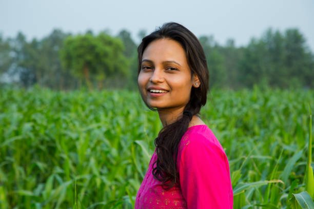 Woman wearing a pink dress smiling while standing in a green field of crops.